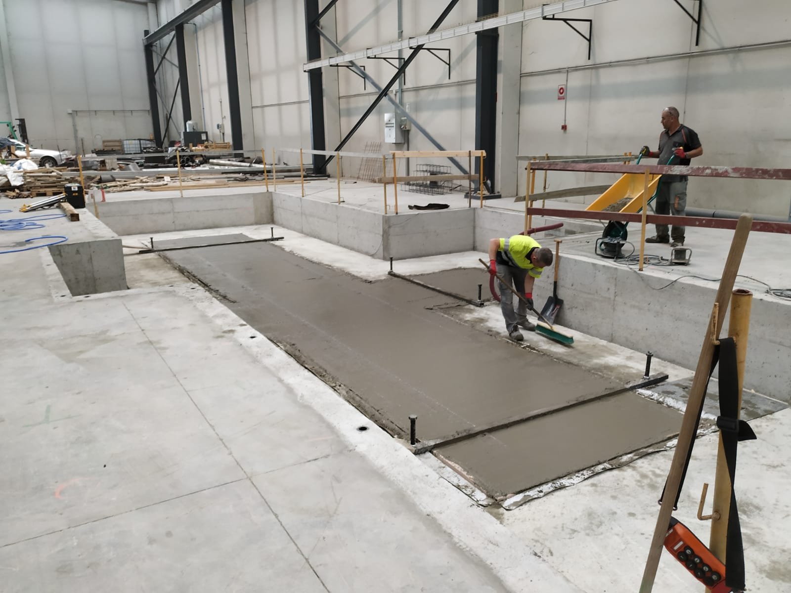 Arbeiter beim Glätten einer Betonsohle im Inneren einer Halle.